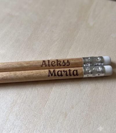 Koka zīmuļi ar gravētu uzrakstu “Prāta vētra 65”, izkārtoti uz apaļa koka dēlīša.