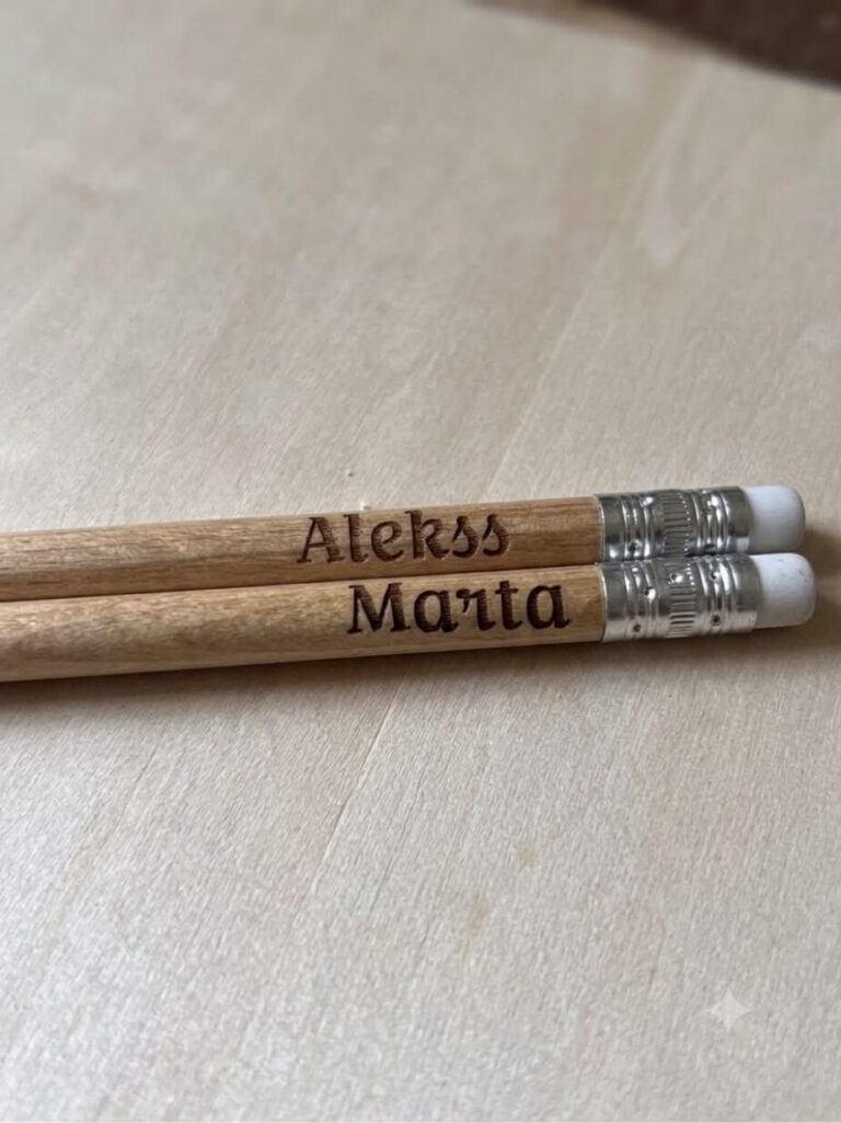 Koka zīmuļi ar gravētu uzrakstu “Prāta vētra 65”, izkārtoti uz apaļa koka dēlīša.