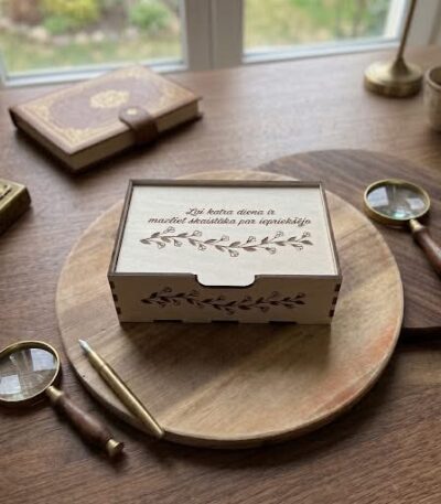Personalizējama koka kastīte ar gravētu uzrakstu un dekoratīvu zaru ornamentu uz vāka, izmērs 20 × 15 × 5 cm.
